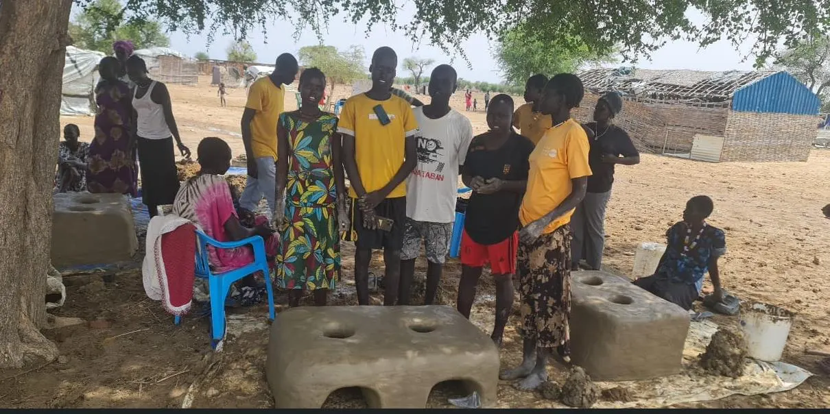 Women and young people gather around freshly moulded stoves during training.