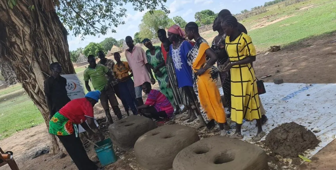 Outdoor stove production training in the shade of a tree.